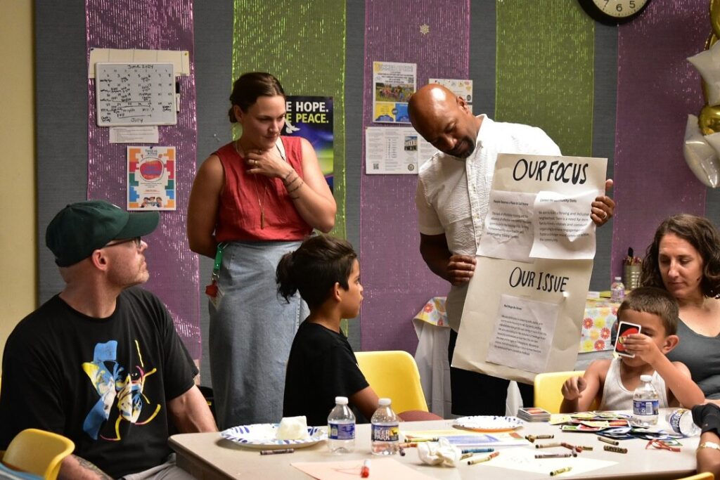 Cohesion Network - instructor holding up "our focus, our issue" posterboard to child in classroom