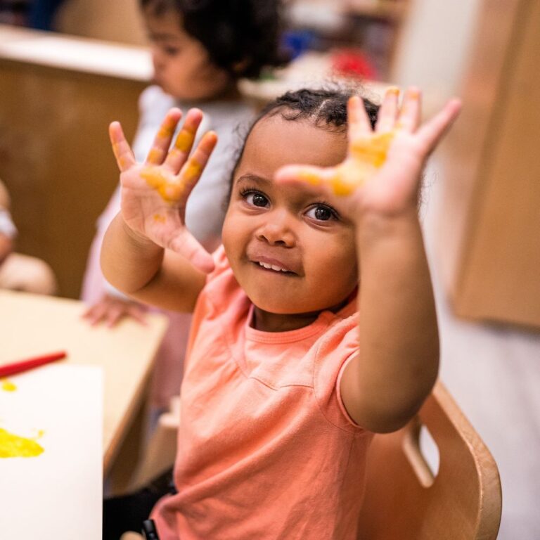 small child holding up her paint-covered hands